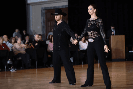 Lucas and Stacey in black outfits standing hand-in-hand on the dance floor