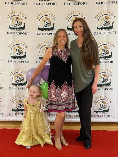 Stacey posing with a student in front of an Invictus Dancesport logo backdrop